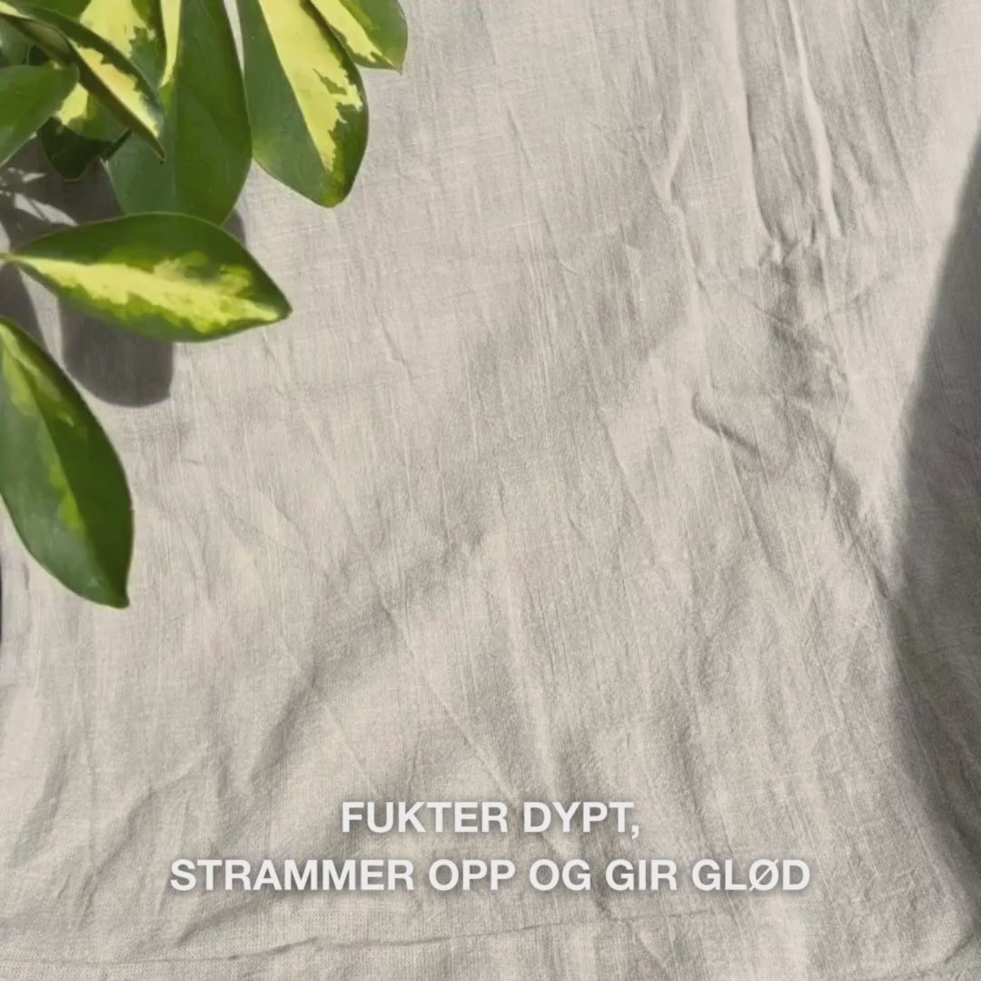 Nærbilde av en kvinne som påfører en knallrosa ansiktsmaske med vitamin B12 og kollagen på renset hud: hun jevner den ut over kinn, panna og hake, mens kollagen- og B12-formelen fukter, styrker, beroliger og gir en glødende hud.