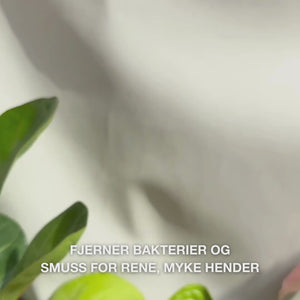 Nærbilde av hender som pumper klar, lyseblå, skummende flytende håndsåpe med Tea Tree Oil i håndflaten og forsiktig skummer den inn på håndflater, håndrygger og mellom fingrene — skummet rengjør bakterier og smuss, samtidig som det mykgjør og fukter huden.
