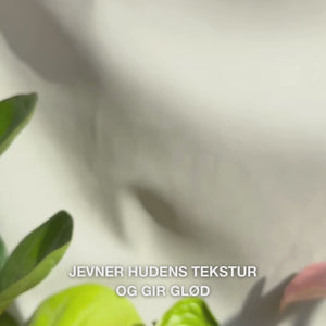 Nærbilde av en hånd som doserer noen tynne dråper av et gjennomsiktig, lett Peeling‑Serum på fingertuppene og masserer det forsiktig inn i ren ansiktshud — den silkemyke, flytende teksturen løser synlig døde hudceller, forfiner hudens struktur og gir glød med naturlige AHA (Lime Pearl), niacinamid og tea tree‑olje 