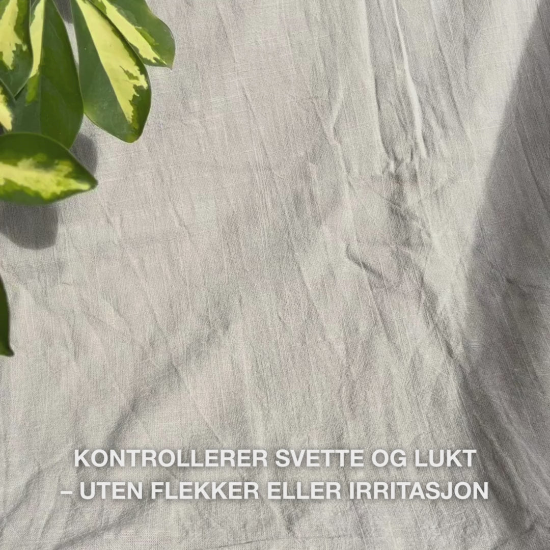Nærbilde av en hånd som ruller den klare, geléaktige deodoranten i roll-on-form på ren hud under armen: den glatte, hurtig­tørkende teksturen glir forsiktig, danner en antiperspirantbarriere, beroliger, fukter og etterlater huden frisk og uten rester.
