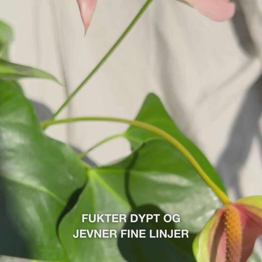 Nærbilde av en hånd som doserer noen dråper silkemyk, klar ansikts‑serum fra en pipette til fingertuppene og masserer den forsiktig inn i lett fuktig hud – den lette og raskt absorberende teksturen gir umiddelbar fukt, fyller fine linjer og beroliger med 2 % hyaluronsyre, vitamin B5 og tea‑tree‑olje 
