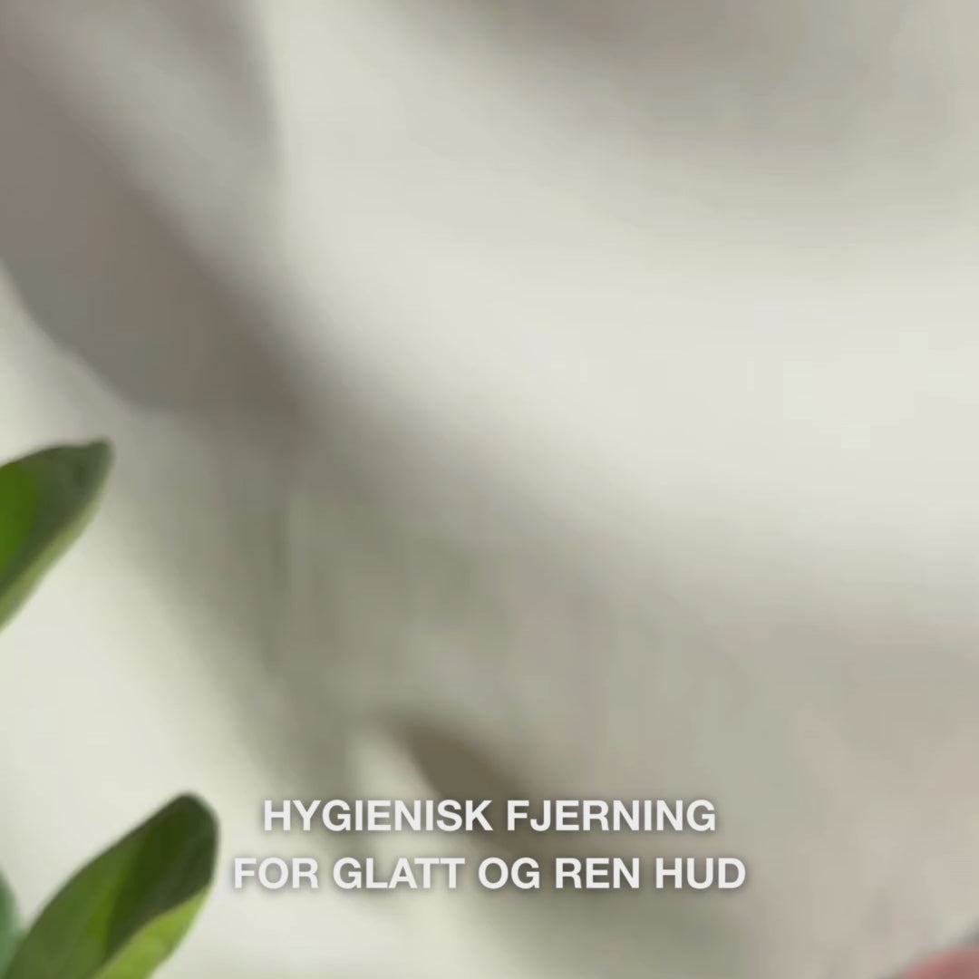 Nærbilde av hender som bruker et tosidig verktøy i rustfritt stål for å fjerne hudormer i ansiktet: en liten metallsløyfe trykkes lett rundt en hudorm på nesen, deretter tørkes det uttrukne talget av, verktøyet skylles, og så påføres en beroligende tonic og ansiktskrem.